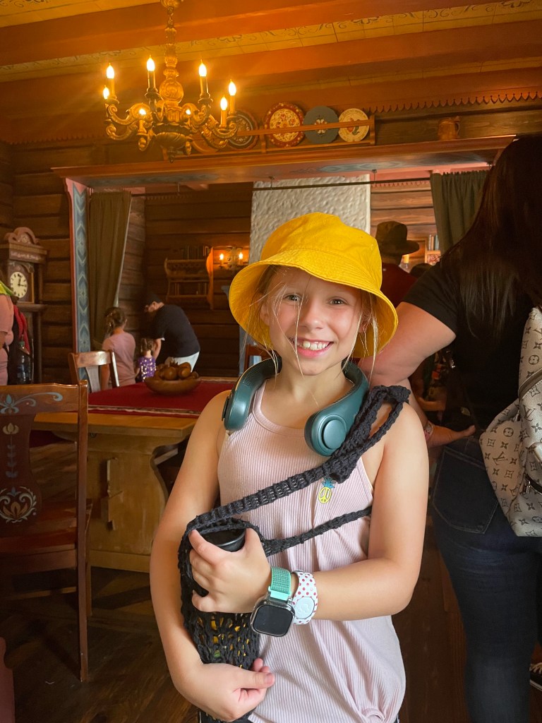 A small child with a yellow hat holds a water bottle encased in a holder made from yarn.